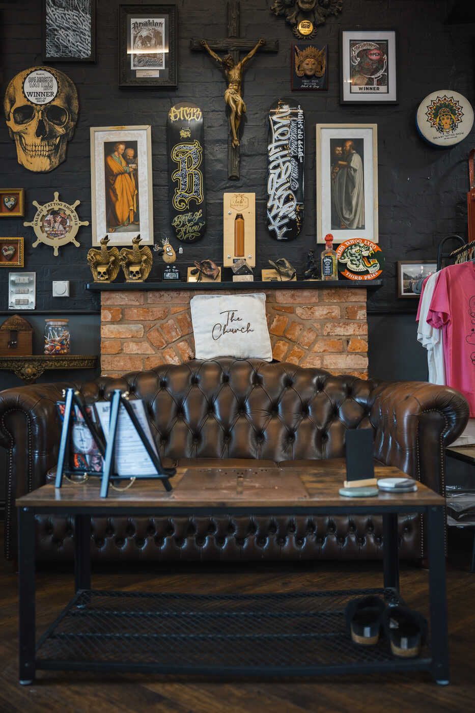 Brand corner of The Church Tattoo Studio — chesterfield sofa, exposed brick, branded cushions.