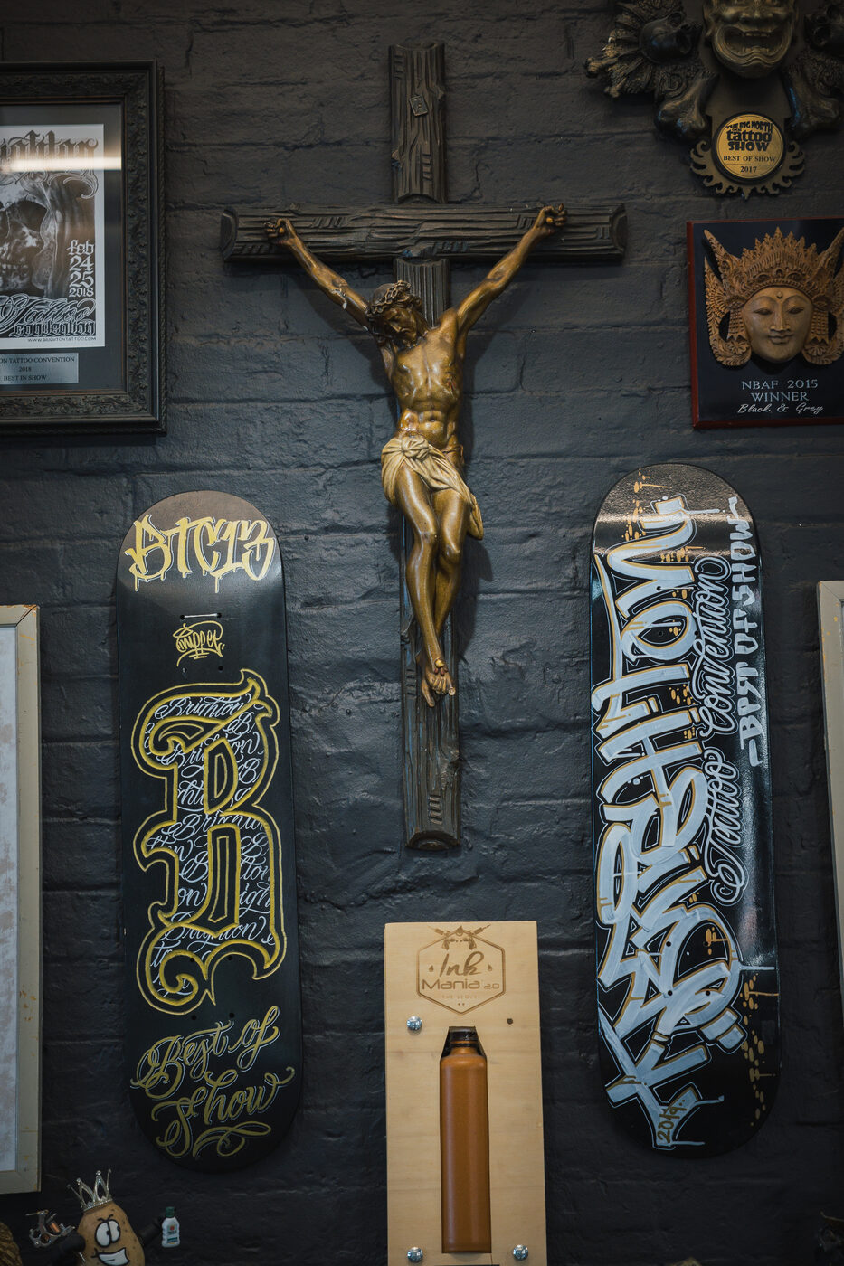 Detail of a brass crucifix flanked by branded skateboards on a dark studio wall.